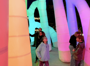 A group of people explores large, colorful, inflatable structures illuminated in vibrant hues at night.
